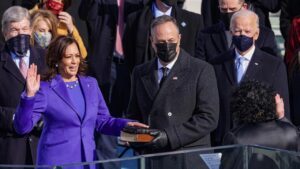 kamala harris in purple jacket raising hand to be sworn in other people with mask stand around her